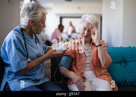 Ältere Frau Klagen über Kopfschmerzen, Arzt während Blutdruck Check-up im Pflegeheim Stockfoto