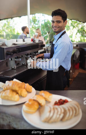 Porträt von lächelnden Kellner Tasse Kaffee aus der Espressomaschine im Restaurant zu machen Stockfoto