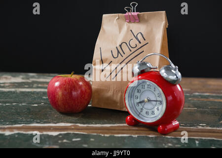 Nahaufnahme von Apple, Wecker und Lunchpaket auf Holztisch Stockfoto