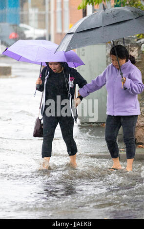 Zwei Frauen zu Fuß durch Flash-Überschwemmungen Wasser auf dem Heimweg nach Starkregen verursachte Sturzfluten, die A525 im Sommer während der Donner und Gewitter, die das Gebiet, Rhyl, North Wales, UK Stockfoto