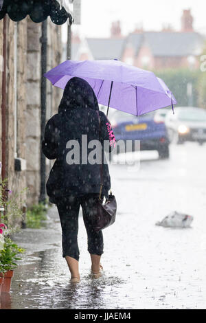 Eine Frau geht durch Flash-Überschwemmungen Wasser auf dem Heimweg nach Starkregen verursachte Sturzfluten, die A525 im Sommer während der Donner und Gewitter, die das Gebiet, Rhyl, North Wales, UK Stockfoto