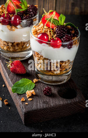 Gesundes Frühstück. Sommer Beeren und Früchte. Hausgemachte griechische Joghurt mit Müsli, Brombeeren, Erdbeeren, Kirschen und Minze. Auf Holz und Stein Stockfoto