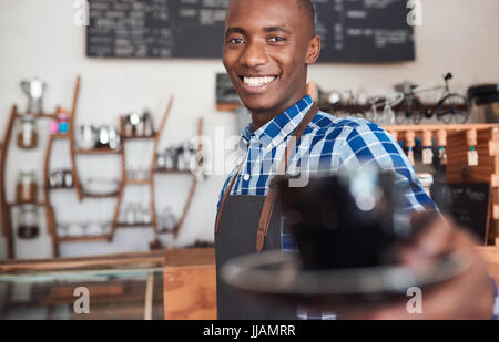 Porträt einer lächelnden afrikanischen Barista stehen an der Theke ein trendiges Café bietet eine frische Tasse cappuccino Stockfoto
