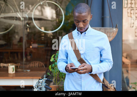 Stilvoll gekleidet junge afrikanische Mann der Straße vor einem Café lesen Text Nachrichten auf seinem Handy Stockfoto