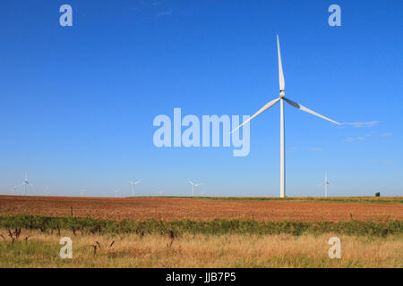 Ein Windpark in Oklahoma erhebt sich über dem roten Boden eines leeren Ernte-Feldes. Stockfoto