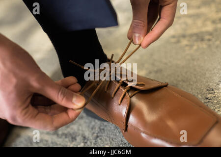 Ein Mann fesselt Gesellschaftskleidung braune Schuhe, wie er gekleidet für Abschlussball bekommt. Ziehen Knoten in Raff Kleidschuhe. Stockfoto