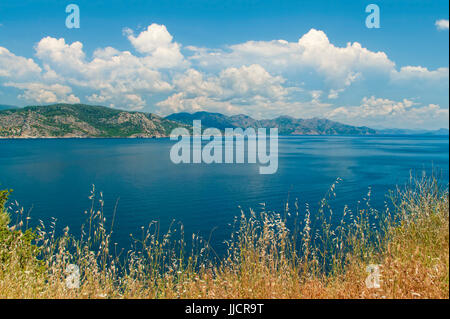 Blick auf die Ägäis mit hohen trockenen gelben Gras im Vordergrund und grünen Bergen und blauem bewölkter Himmel im Hintergrund in Amos Bay, Mugla, Türkei Stockfoto