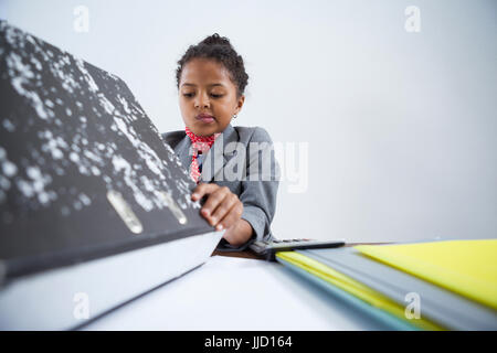 Mädchen, so zu tun als Geschäftsfrau arbeiten beim Sitzen am Schreibtisch vor weißem Hintergrund Stockfoto