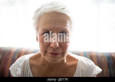 Close-up Portrait senior Frau sitzend auf Sofa gegen Fenster im Altersheim Stockfoto