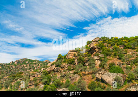 Grosse Felsen und Bäume mit gelben Blumen an der Seite des Berges, auf sonnigen Tag gegen den schönen blauen Himmel mit Wolken in der Türkei Stockfoto