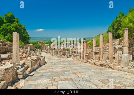 Marmor-Gasse mit Spalten, was zu der Celsus-Bibliothek in der antiken griechischen Stadt Ephesus mit Bergen und klaren blauen Himmel im Hintergrund mit einzelnen s Stockfoto