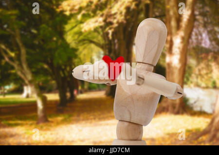 Hölzerne 3D-Figur stehen und hält ein rotes Herz vor gegen Reihe von Bäumen im park Stockfoto