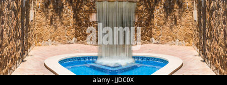 Luxus Swimmingpool mit Wasserfall. Im Hintergrund ein mediterranes Wand dekoriert mit Sandsteine Stockfoto