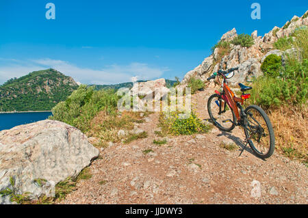 Orange Mountain Bike stehend auf dem felsigen Gipfel Barths Ägäischen Meer am Tag Sunne, Marmaris, Türkei Stockfoto