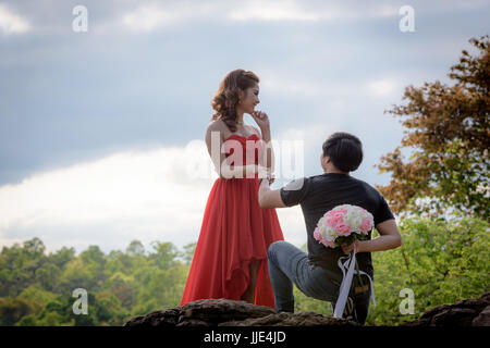 Junger Mann einen Blumenstrauß hinter ihm verstecken soll eine junge Frau im roten Kleid zu liefern. Stockfoto