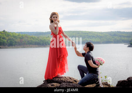 Junger Mann einen Blumenstrauß hinter ihm verstecken soll eine junge Frau im roten Kleid zu liefern. Stockfoto