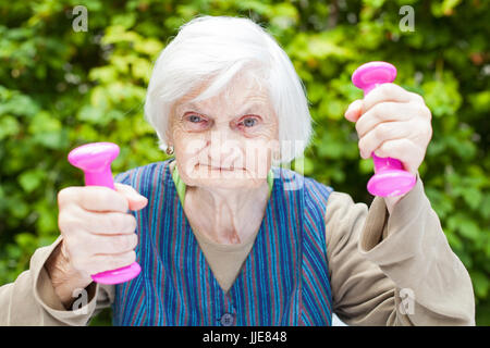 Bild des erregten ältere Frau sport Übungen im Freien im Garten, Holding rosa Hanteln Stockfoto