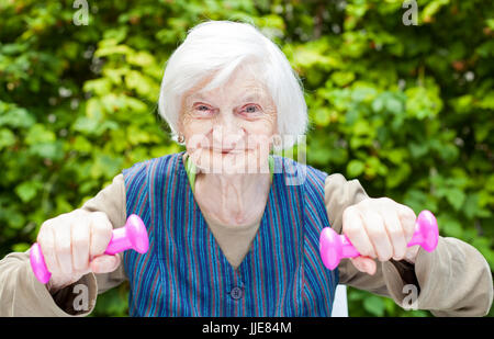 Bild des erregten ältere Frau sport Übungen im Freien im Garten, Holding rosa Hanteln Stockfoto
