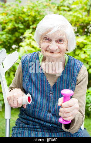 Bild des erregten ältere Frau sport Übungen im Freien im Garten, Holding rosa Hanteln Stockfoto