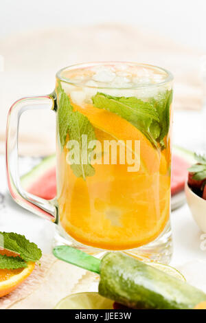 ein Glas mit einem erfrischenden Getränk, mit Orangenscheiben und Minze, eine Schale mit Erdbeeren, eine Platte mit Wassermelone und ein Teller mit einigen verschiedenen hausgemachten Stockfoto