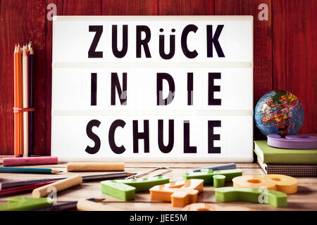 der Text zurück in Die Schule, zurück zur Schule in deutscher Sprache in einer Lightbox, einem rustikalen hölzernen Hintergrund platziert umgeben von dreidimensionalen taub Stockfoto