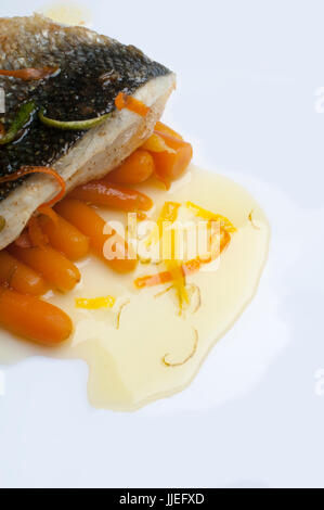 Wolfsbarsch (Dicentrarchus Labrax) mit frischem Baby-Karotten in einer Zitronensauce auf einem weißen Teller. Stockfoto