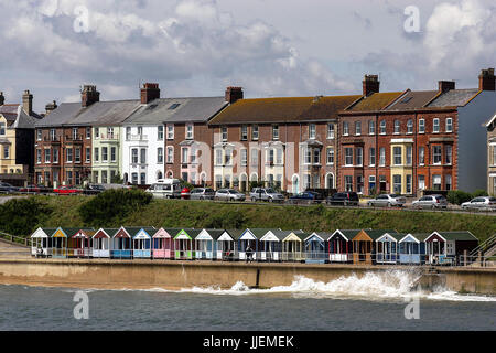 Eine Reihe von typisch britischen Strandhütten auf der Ufermauer imitiert die Reihenhäuser der Stadt über, als die Flut Surf wäscht die Vorderseite. Stockfoto