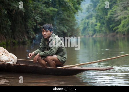 Ein junger Mann auf eine Jagd und Fischfang-Expedition raucht eine Zigarette in seinem Einbaum-Boot am Fluss Nam Ou, Laos. Stockfoto