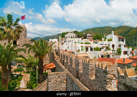 Blick auf Marmaris Schloss mit türkischer Flagge und weißen Häusern in der Altstadt mit grünen Bergen im Hintergrund an sonnigen Tag gegen blauen Himmel, Marmaris, Tur Stockfoto