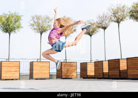 Aktives Kind Mädchen Turnerin springen oder tanzen auf der Straße. Junges Mädchen Acrobat. Das Mädchen beschäftigt sich mit Gymnastik. Stockfoto