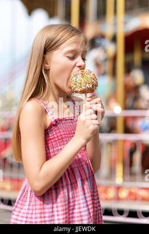 Niedliche kleine Mädchen essen Liebesapfel auf Messe im Vergnügungspark. Stockfoto
