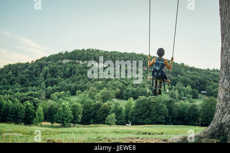 Eine weibliche Wanderer ist auf einer Schaukel im Wald mit Blick auf die Berge. Stockfoto