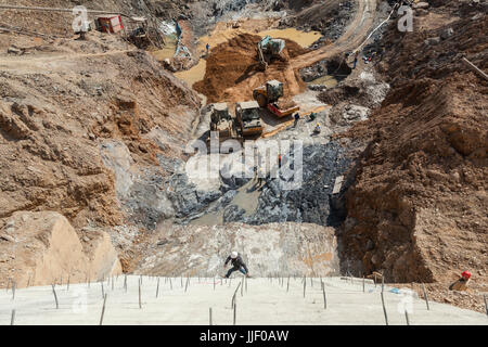 Ein Bauarbeiter durchläuft eine senkrechte Wand durch den Ausbau auf hervorstehende Bewehrung über Erdarbeiten an der Baustelle für Dam #5 auf dem Nam Ou Fluss in Laos. Stockfoto