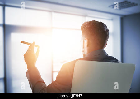 Rückansicht der Geschäftsmann mit Zigarre gegen innere des modernen Büros Stockfoto