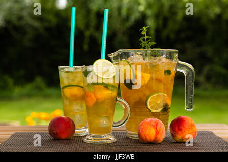Hausgemachte peach Ice grüner Tee mit Kalk und Zitronenmelisse. Auf einer hölzernen Tisch draußen im Garten. Gesunde Getränke Konzept. Stockfoto
