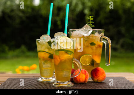 Hausgemachte peach Ice grüner Tee mit Kalk und Zitronenmelisse. Auf einer hölzernen Tisch draußen im Garten. Gesunde Getränke Konzept. Stockfoto