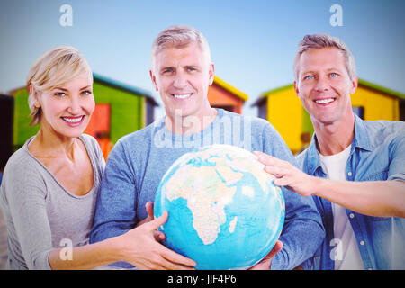 Porträt von Menschen halten Globus gegen Multi farbige Hütten auf Sand gegen klaren Himmel Stockfoto