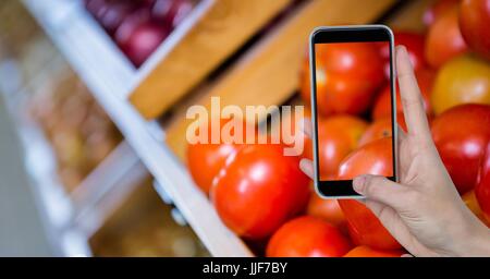 Digitalen Verbund von Hand unter Bild von Tomaten durch Smartphone an Lebensmittelgeschäft Stockfoto