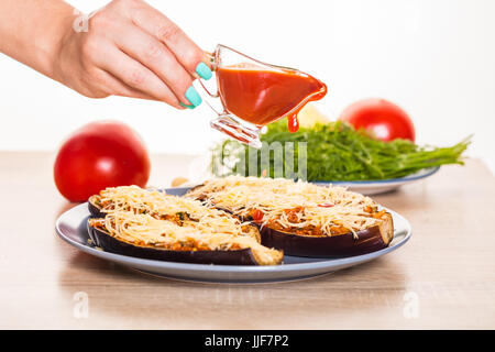 Cook gießt Tomatensauce auf gefüllte Auberginen Stockfoto