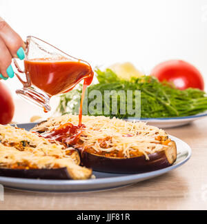 Cook gießt Tomatensauce auf gefüllte Auberginen Stockfoto