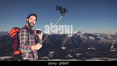 Digital Composite Hipster Rucksack mit Kamera und nehmen Selfie stehend gegen Berge Stockfoto