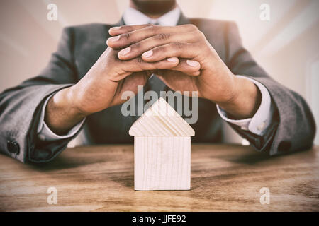 Geschäftsmann Hausmodell mit Händen gegen hellen weißen Raum zu schützen Stockfoto