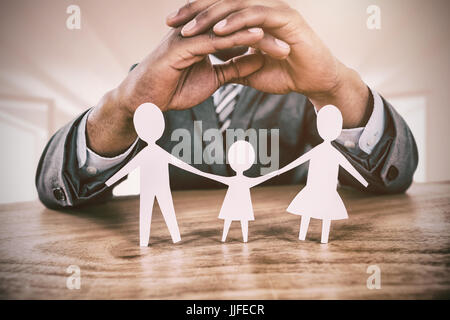 Hand zum Schutz einer Familie in Papier gegen hellen weißen Raum mit geöffneten Fenstern Stockfoto