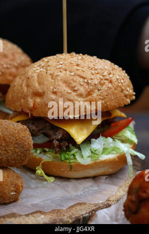 Big American Cheeseburger mit gezogenes Schweinefleisch und Salat in Sesam Brötchen auf Pergament Papier über natürliche Holz geschnitten, Nahaufnahme, niedrigen Winkel Ansicht Stockfoto