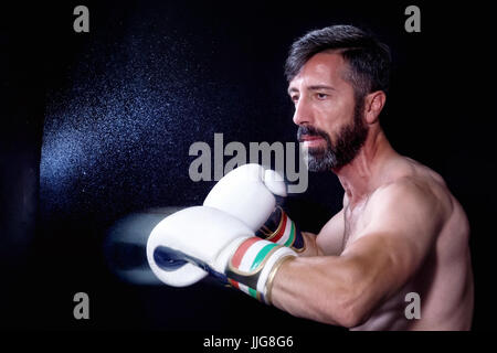 Männer-Boxer aus einen Schlag in der Plünderung. Spritzer von Wasser und Schweiß auf dem schwarzen Hintergrund. Stockfoto