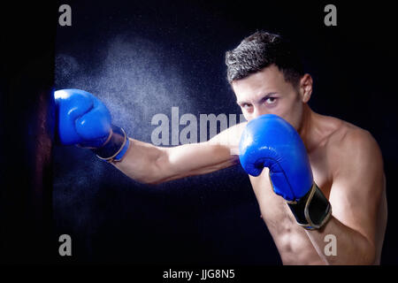 Junge Boxer aus einen Schlag in der Plünderung. Spritzer von Wasser und Schweiß auf dem schwarzen Hintergrund. Stockfoto