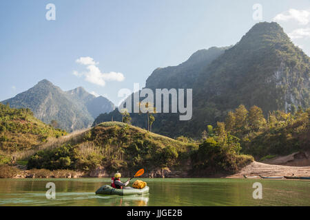 Robert Hahn paddelt seine Packraft unter dramatischen Karstgebirge erhebt sich über ihm auf dem Nam Ou Fluss in der Nähe von Muang Ngoi, Laos. Stockfoto