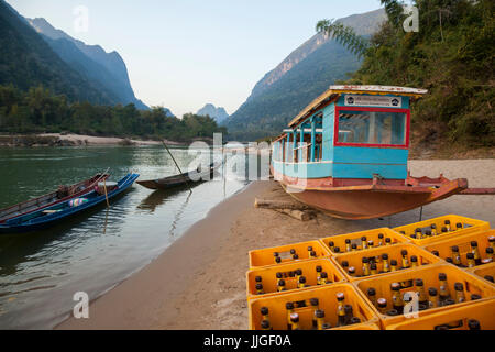 Boote und einen großen Stapel von leeren Beer Lao (nationales Bier) am Ufer des Flusses Nam Ou in Muang Ngoi, Laos. Das Bier ist notwendige Brennmaterial für den lebendigen Tourismus rund um die Stadt zentriert. Stockfoto