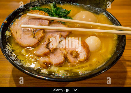 Leckere japanische Ramen-Nudeln mit Stäbchen über die Suppe in einem hölzernen Hintergrund. Stockfoto