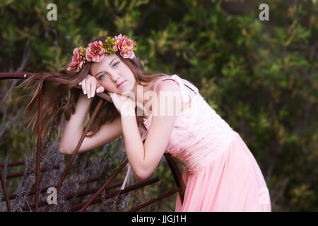 Mädchen in einem rosa Kleid, das sich an einem alten rostigen Wagenrad lehnt, Kalifornien, USA Stockfoto